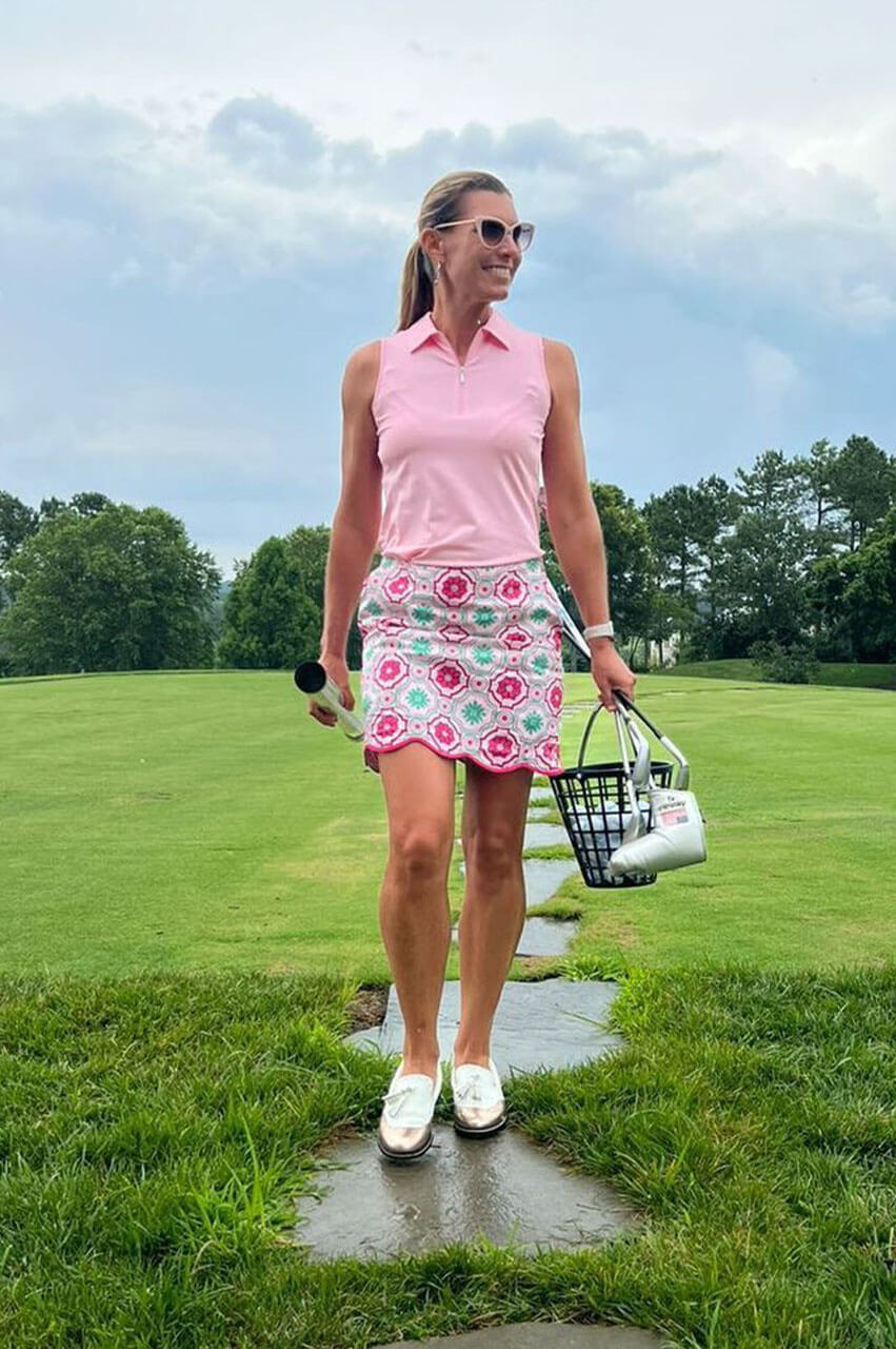 Female golf instructor in cute pink golf outfit by Golftini going to practice her game at the driving range