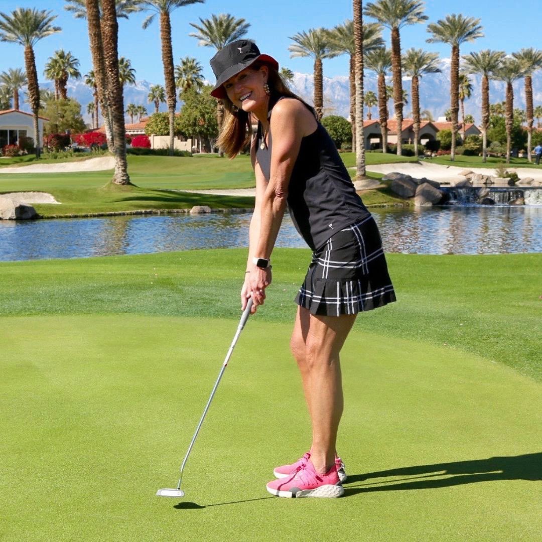 A woman standing on green grass while playing golf. 