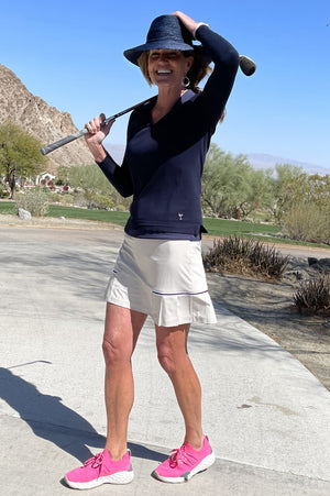 Woman golfing in navy stretch golf sweater and light khaki golf skort.
