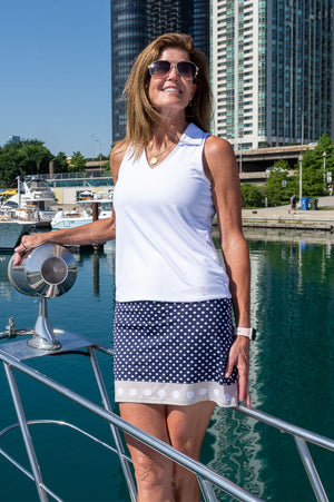 Designer wearing navy polka dot golf skort with a sleeveless white sport polo on a boat in the summer